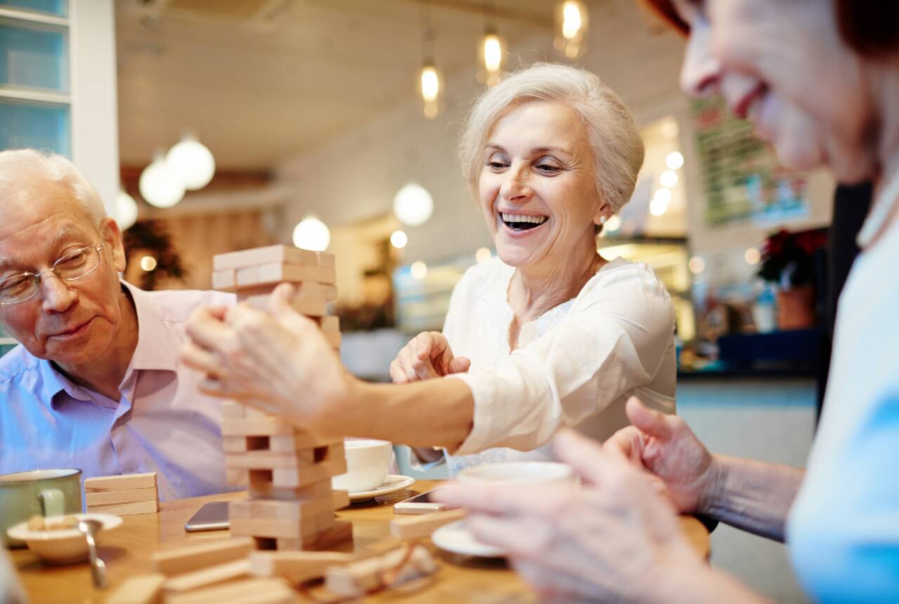 Na fotografii starsi, uśmiechnięci ludzie grający w grę z drewnianych klocków jenga. 