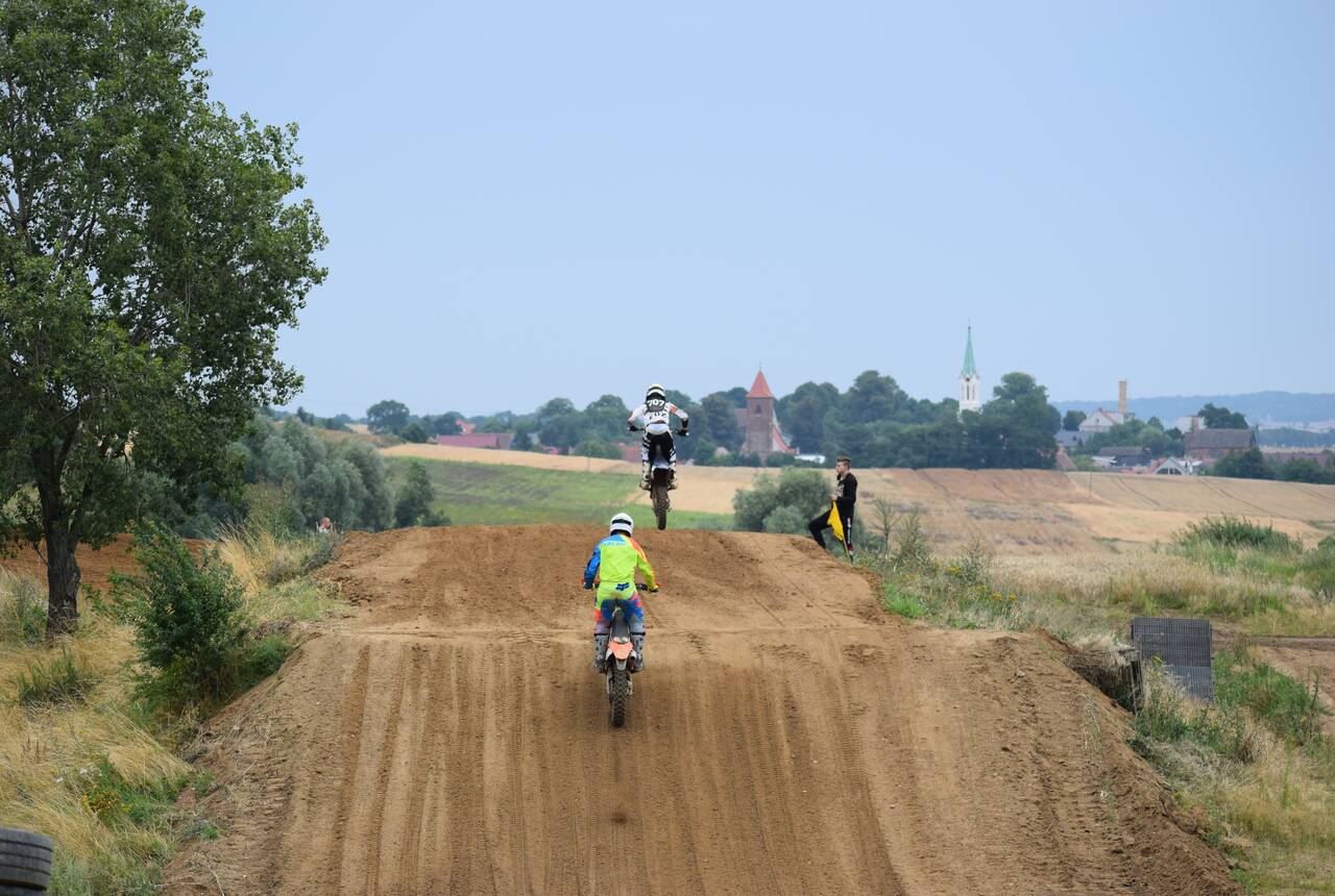 Zdjęcie z zawodów na torze motocrossowym 2021. Na zdjęciu trzech motocyklistów. W oddali widać Gaworzyce.