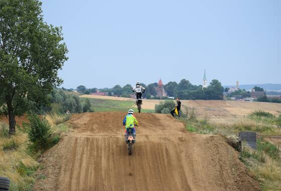 Zdjęcie z zawodów na torze motocrossowym 2021. Na zdjęciu trzech motocyklistów. W oddali widać Gaworzyce.